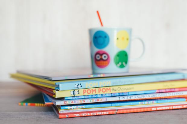 Barrhead News: Children's books in a pile with a colourful mug on top. Credit: Canva
